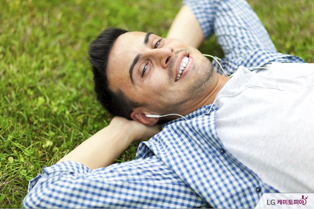 남성이 잔디 위에서 음악을 들으며 미소를 짓고 있다