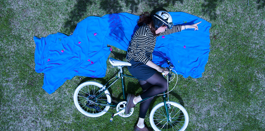 잔디밭에 파란 천을 깔고 자전거를 눕힌 채 올라탄 여자의 사진