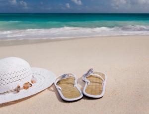 푸른 바다가 보이는 해변 모래 위에 모자와 슬리퍼가 놓여있다