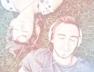 이어폰을 낀 남자와 여자가 잔디밭에 누워서 음악을 듣고 있다.