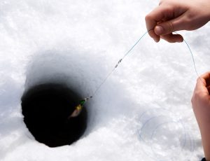 얼음 낚시 구멍에 낚시 줄을 넣고 있다.